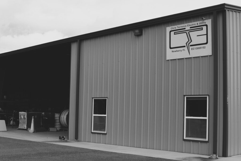 black and white photo of outside of metal building with the Chris Torrence Electric & Utility Logo on the Side.